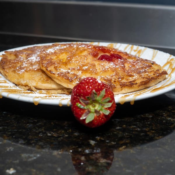 Chef Reeky's Cafe & Juice Bar's pancakes with powdered sugar, syrup, strawberry jam, and a fresh strawberry.