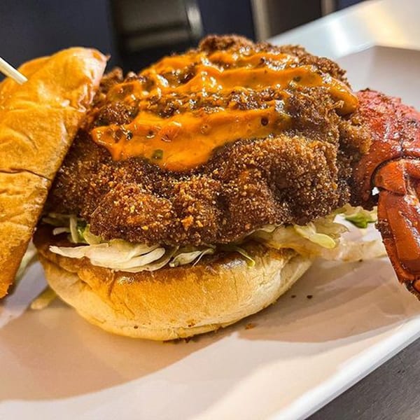 A fried chicken sandwich with orange sauce and a lobster claw on a white plate.